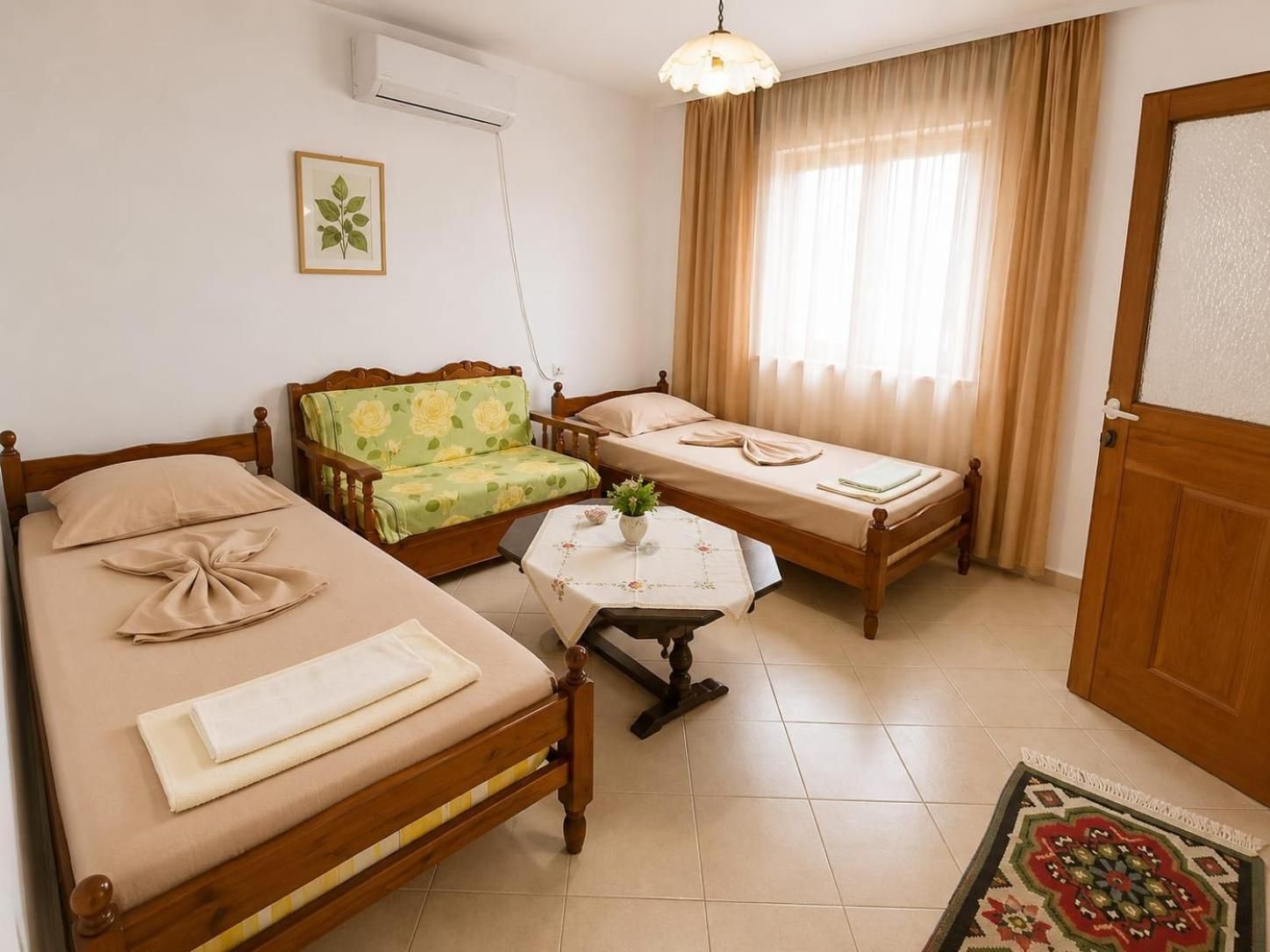 Une chambre avec deux lits simples, un canapé, une petite table avec un vase et une fenêtre avec des rideaux.