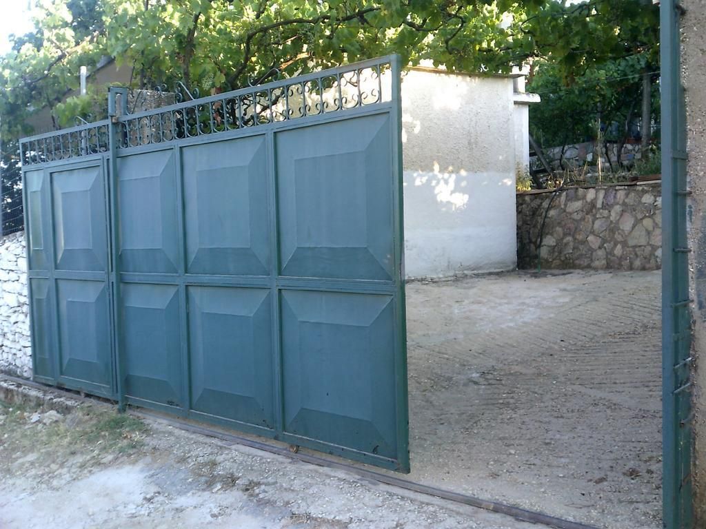 A metal gate with a geometric design, a paved area in front, and a stone wall in the background.