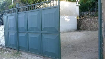 A metal gate with a geometric design, a paved area in front, and a stone wall in the background.