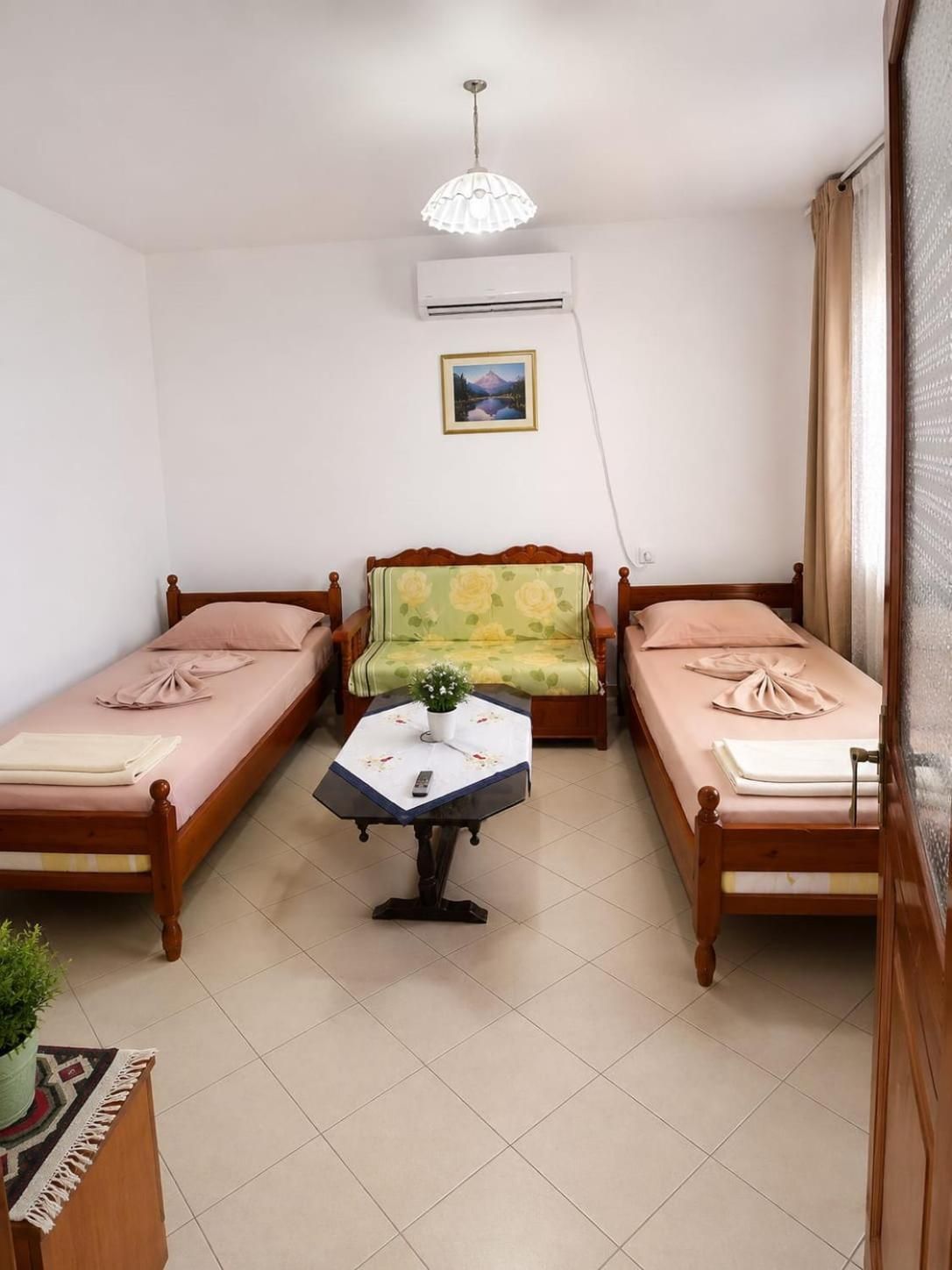 A room with two single beds, a small table with a remote control, and a ceiling light fixture.