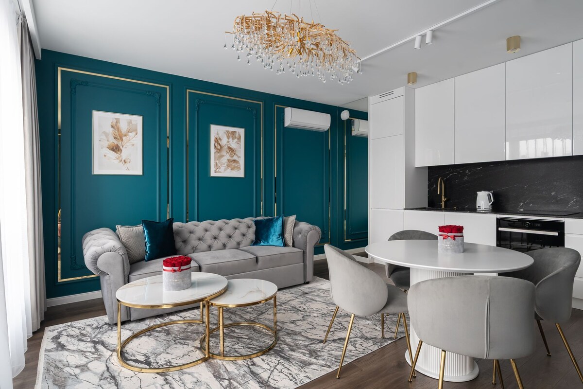 Ein modernes Wohnzimmer mit türkisfarbenen Wänden, einem grauen Sofa und einem runden Esstisch mit Stühlen.