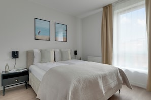 A hotel room with a bed, bedside tables, a nightstand, a radiator, and two framed pictures on the wall. - Scala Suites F with Parking (Gdańsk)