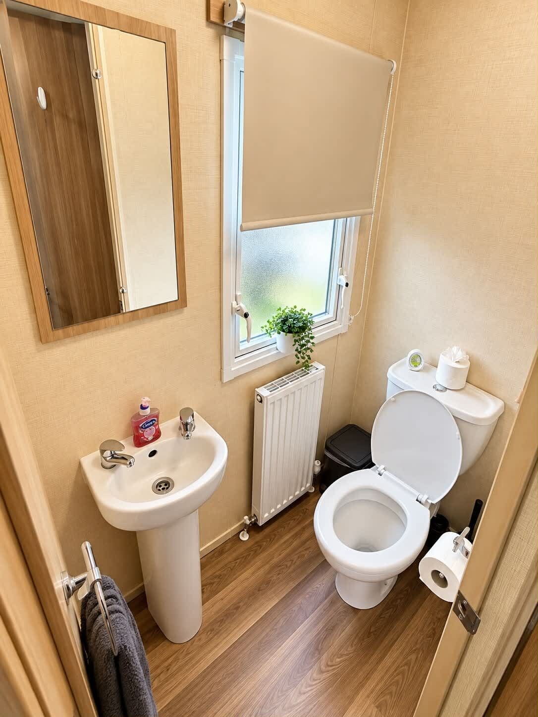 Un baño pequeño con lavamanos, inodoro y ventana con planta.