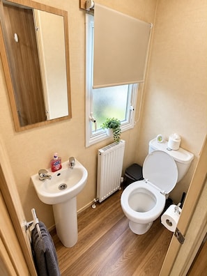 Ein kleines Badezimmer mit Waschbecken, Toilette und einem Fenster mit Pflanze.