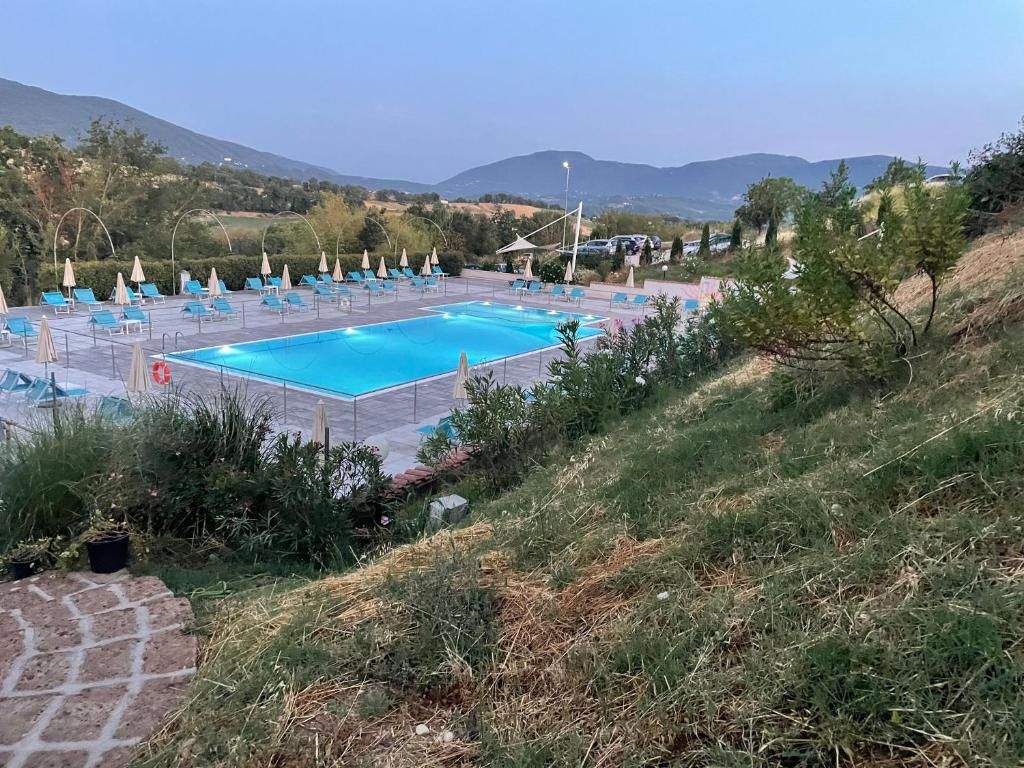 Une piscine entourée de verdure et de collines, avec des chaises longues et des parasols.