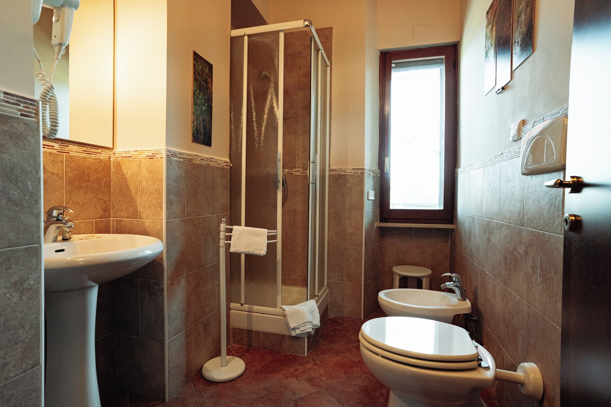 Une salle de bain avec une douche, un lavabo, des toilettes et une petite fenêtre.