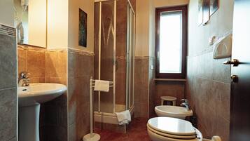 Une salle de bain avec une douche, un lavabo, des toilettes et une petite fenêtre.