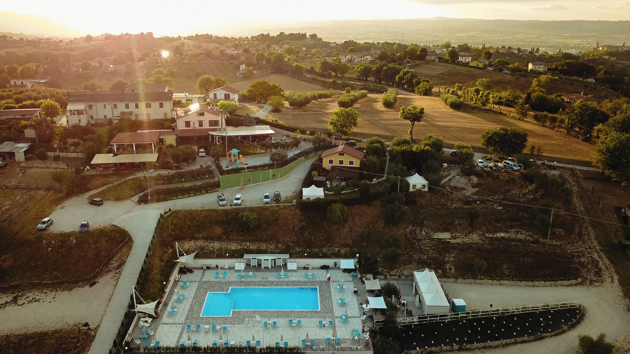 An aerial view of a resort with a swimming pool, multiple buildings, and surrounding greenery.