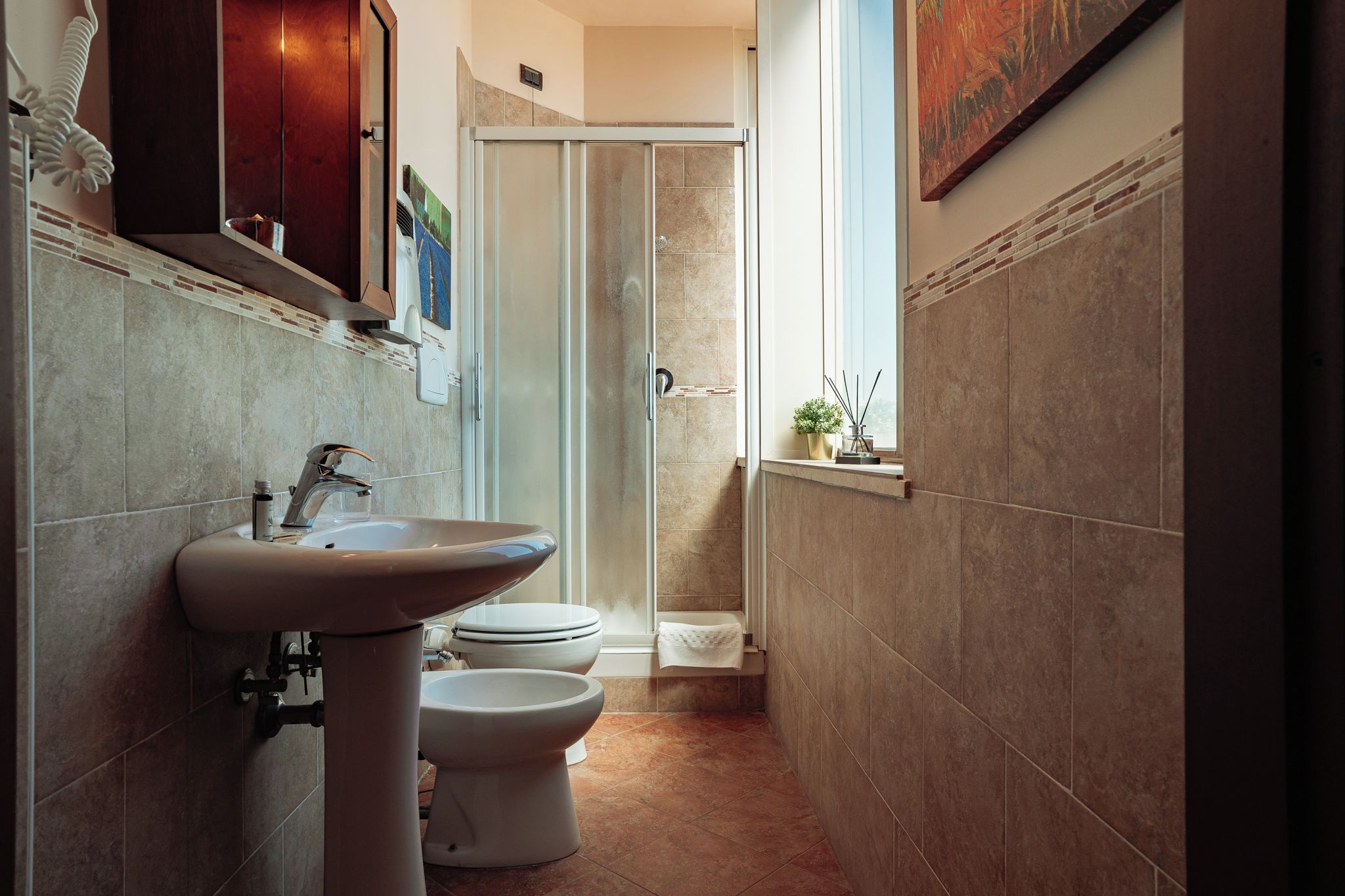 Een badkamer met een wastafel, twee toiletten, een douche en een raam.