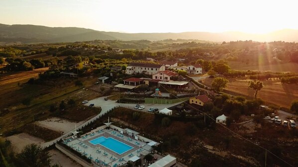 An aerial view of a property with a swimming pool, multiple buildings, and surrounding landscape.