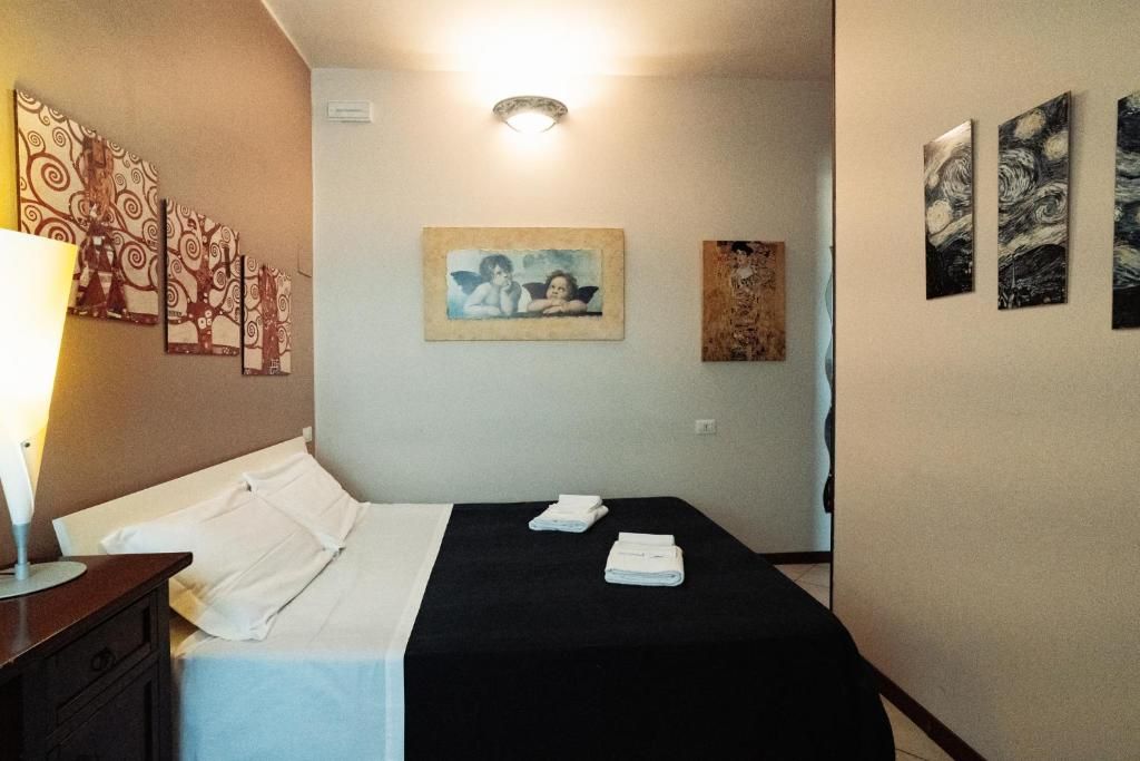 A hotel room with a bed, a nightstand, a lamp, and artwork on the walls.