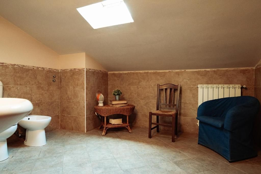 Un baño con inodoro, bidé, una silla, una mesita con una planta y un radiador.