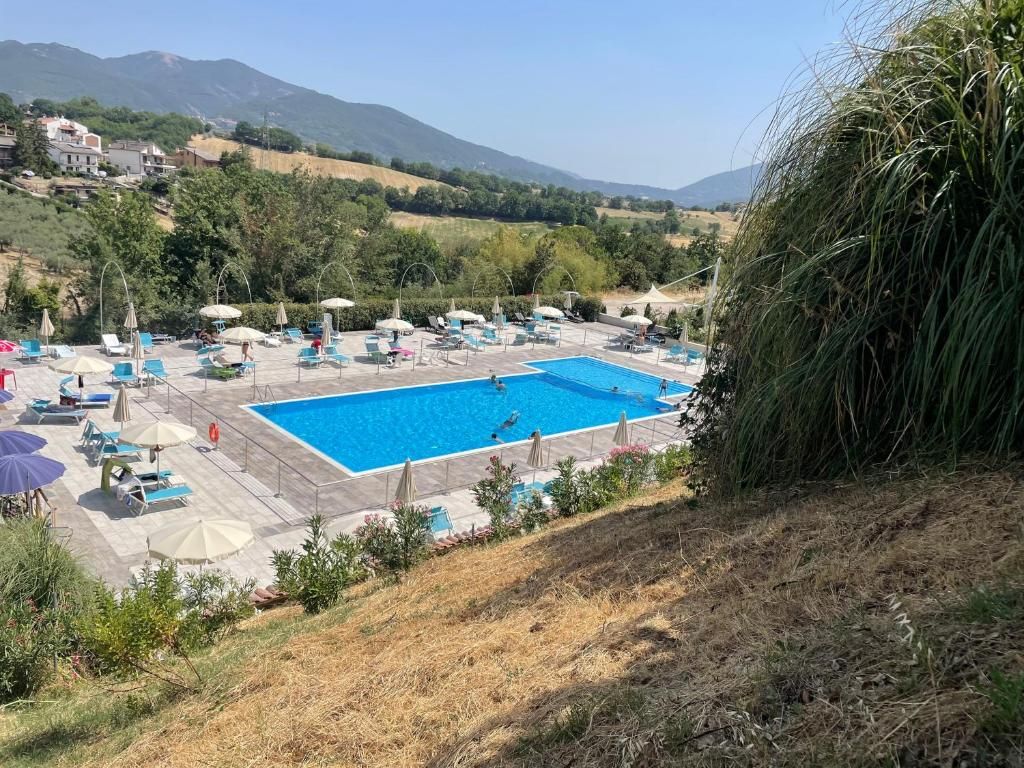 Zona de piscina con sillas de descanso y sombrillas, rodeada de vegetación y montañas al fondo.
