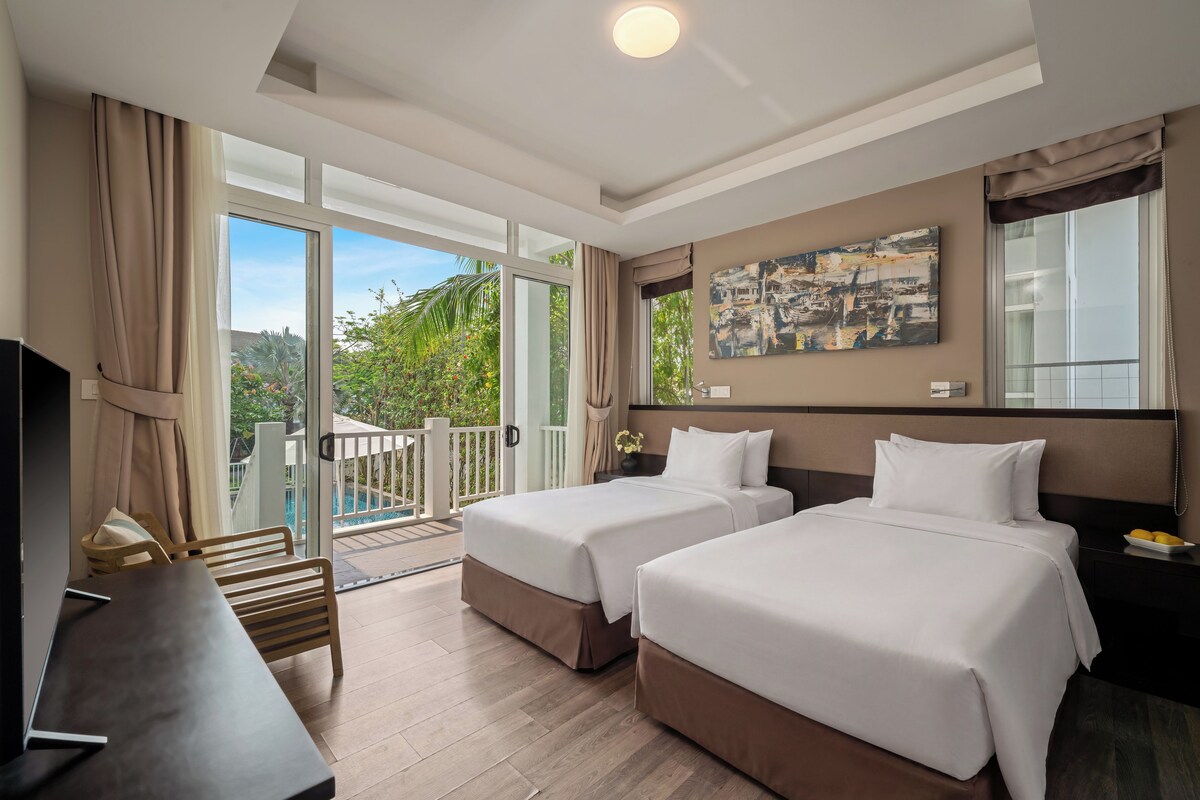 Ein Hotelzimmer mit zwei Betten, einem Schreibtisch, einem Fernseher und einem Balkon mit Blick auf den Pool.