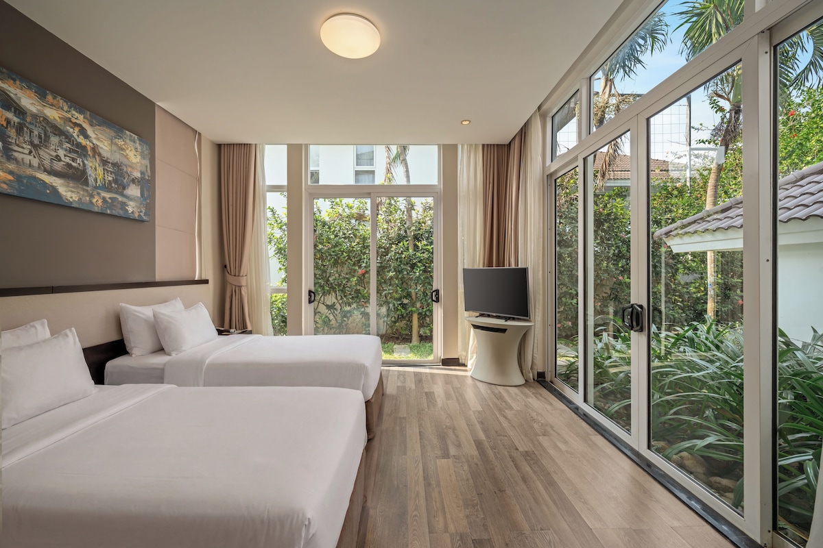 Ein Hotelzimmer mit zwei Betten, einem Fernseher und großen Fenstern mit Blick auf Grünflächen.
