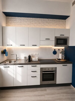 A modern kitchen with white cabinets, stainless steel appliances, and a blue accent wall. - BLUVIA RESIDENCES Spiral Apartment | 2 Minutes to the Train Station | Cinque Terre (La Spezia)