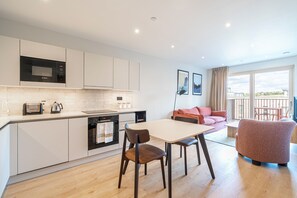 A modern kitchen with a microwave, toaster, and oven. There is a dining table with chairs and a sofa in the living area. - The Sunlit Nook in London (London)
