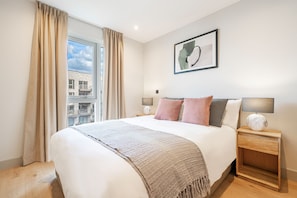 A hotel room with a large bed, a window with curtains, a bedside table with a lamp, and a framed picture on the wall. - The Sunlit Nook in London (London)