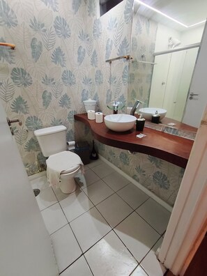 A bathroom with a toilet, a sink, a mirror, and a shower area. - Luxuoso, vista para o Mar (Maceió)