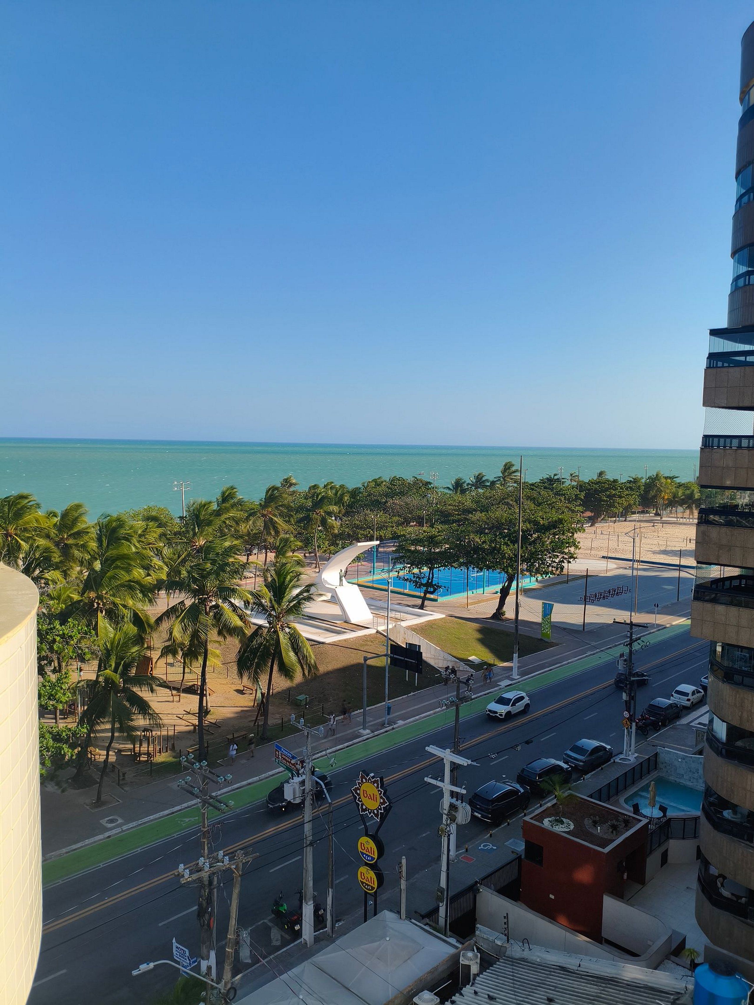 A coastal cityscape with a view of the ocean, palm trees, and a modern building.