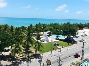 A coastal road with a view of the ocean, palm trees, and a parking area. - Luxuoso, vista para o Mar (Maceió)