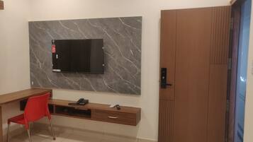 Une chambre moderne avec un téléviseur à écran plat fixé sur un mur de marbre, un bureau en bois avec une chaise rouge et une porte coulissante en bois.