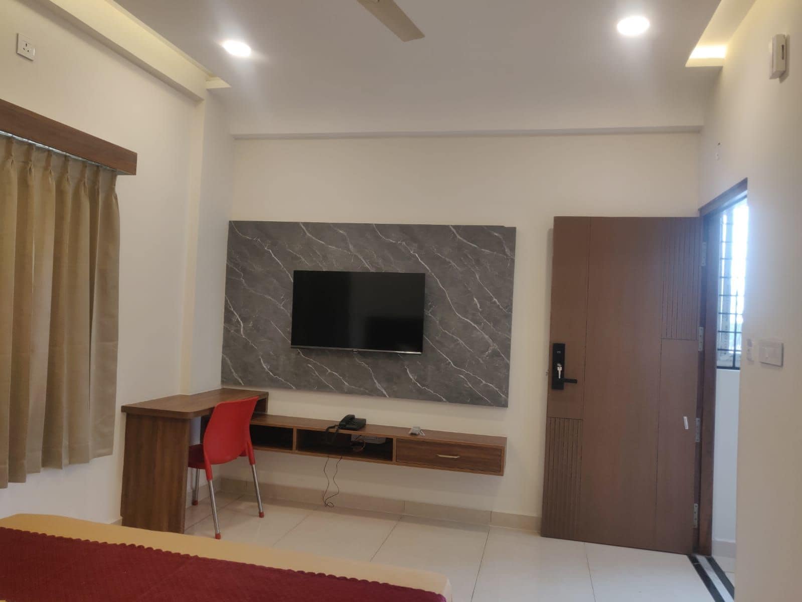 Une chambre moderne avec un téléviseur fixé au mur en marbre, un bureau avec une chaise et une armoire.