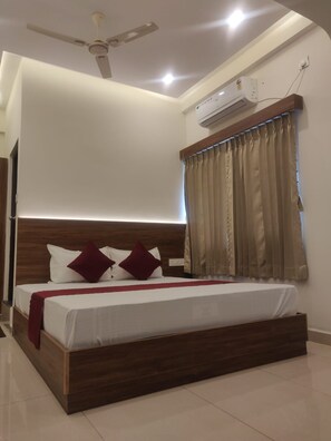 Un dormitorio con cama, ventilador de techo, equipo de aire acondicionado y ventana con cortinas.