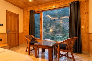 A wooden-paneled room with a large window, two wooden chairs, a small table, and a bed.