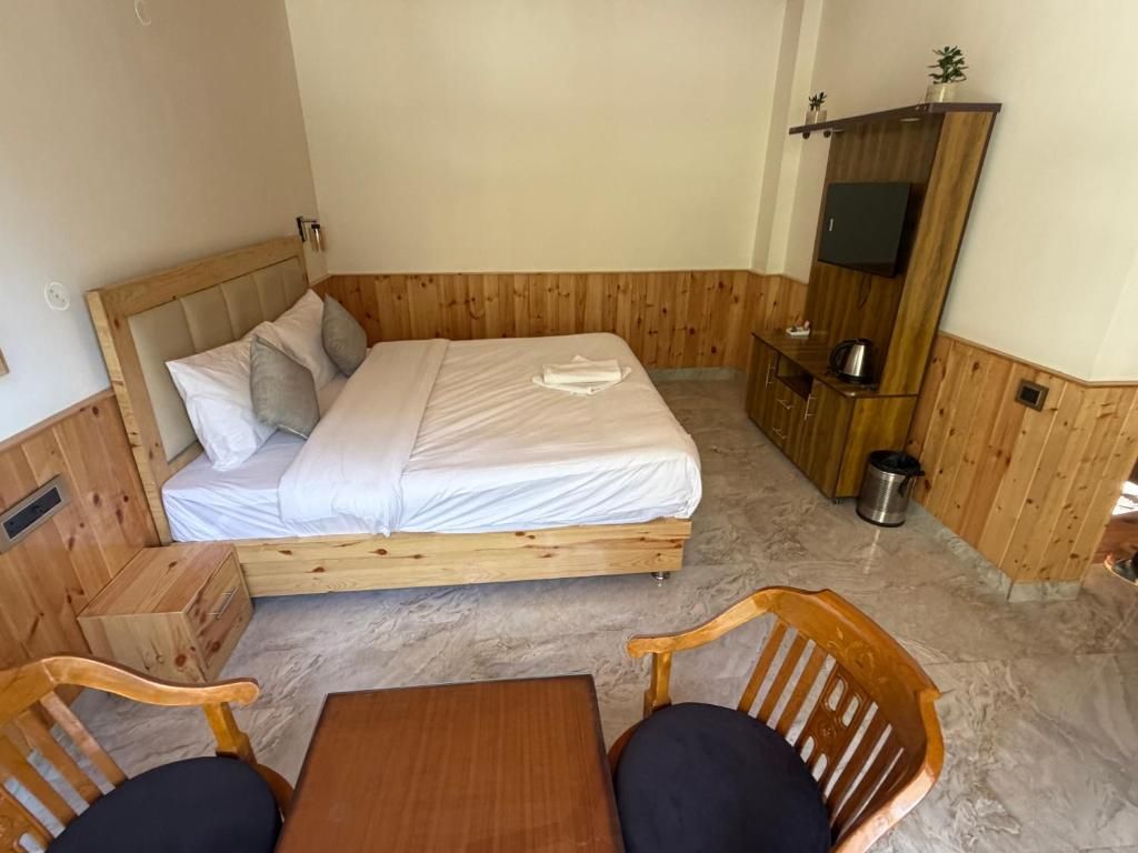 A wooden-paneled room with a bed, a TV, a small table, and two chairs.