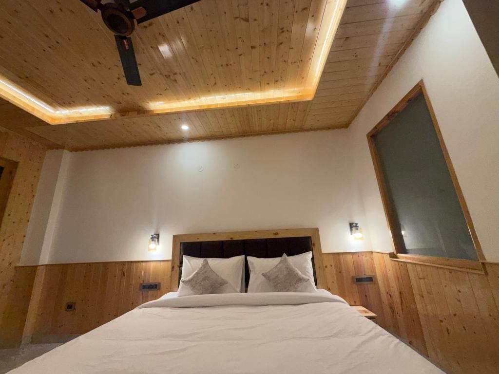 A bedroom with a wooden ceiling, a bed with white bedding, two wall-mounted lights, and a window.