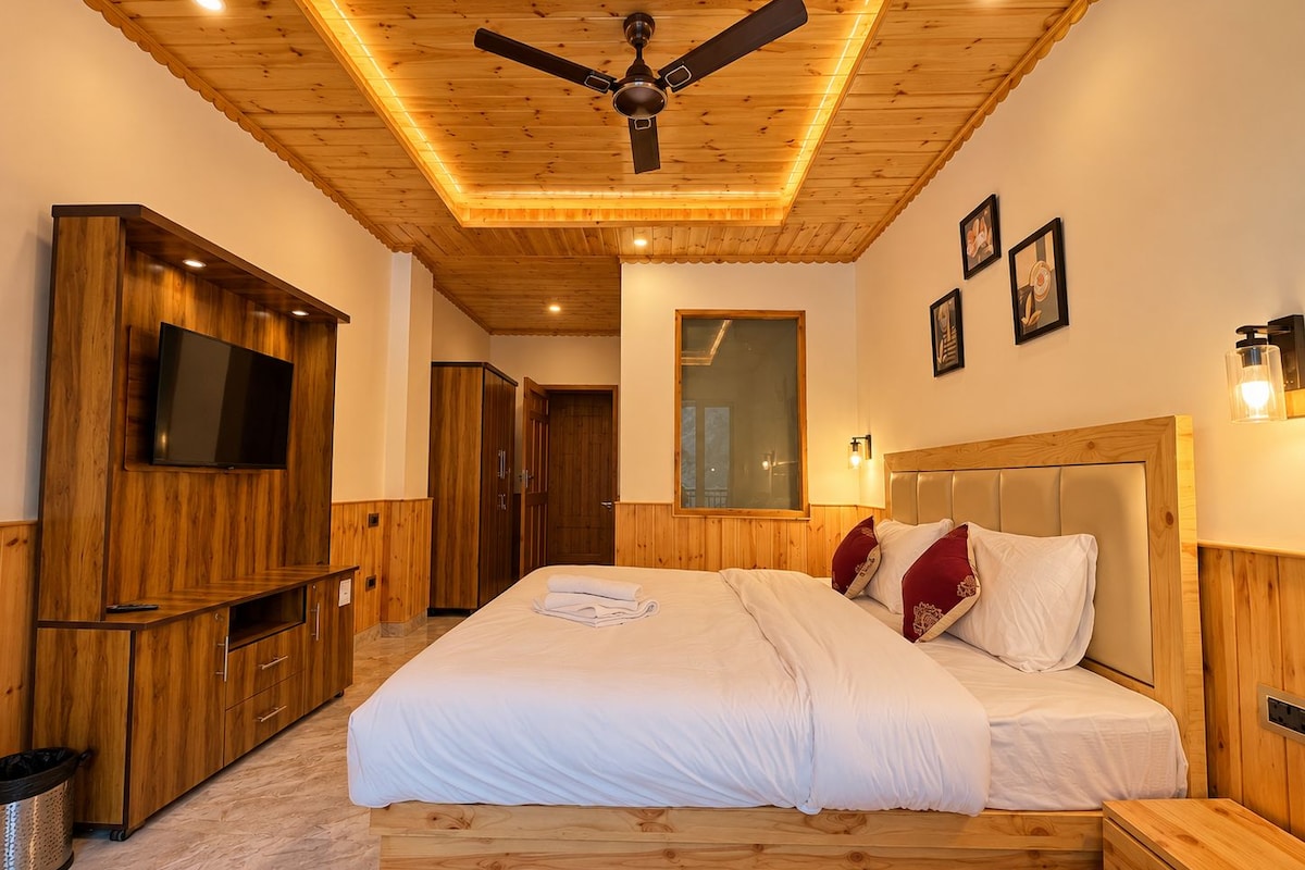 A bedroom with a wooden ceiling, a bed with white bedding, a TV mounted on a wooden cabinet, and a ceiling fan.