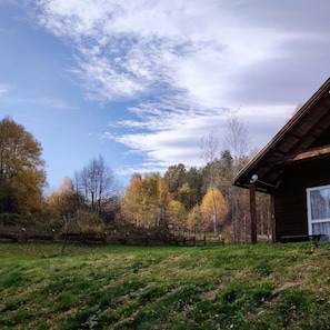Eine Holzhütte mit geneigtem Dach, umgeben von einer Wiese und Bäumen im Herbstlaub.