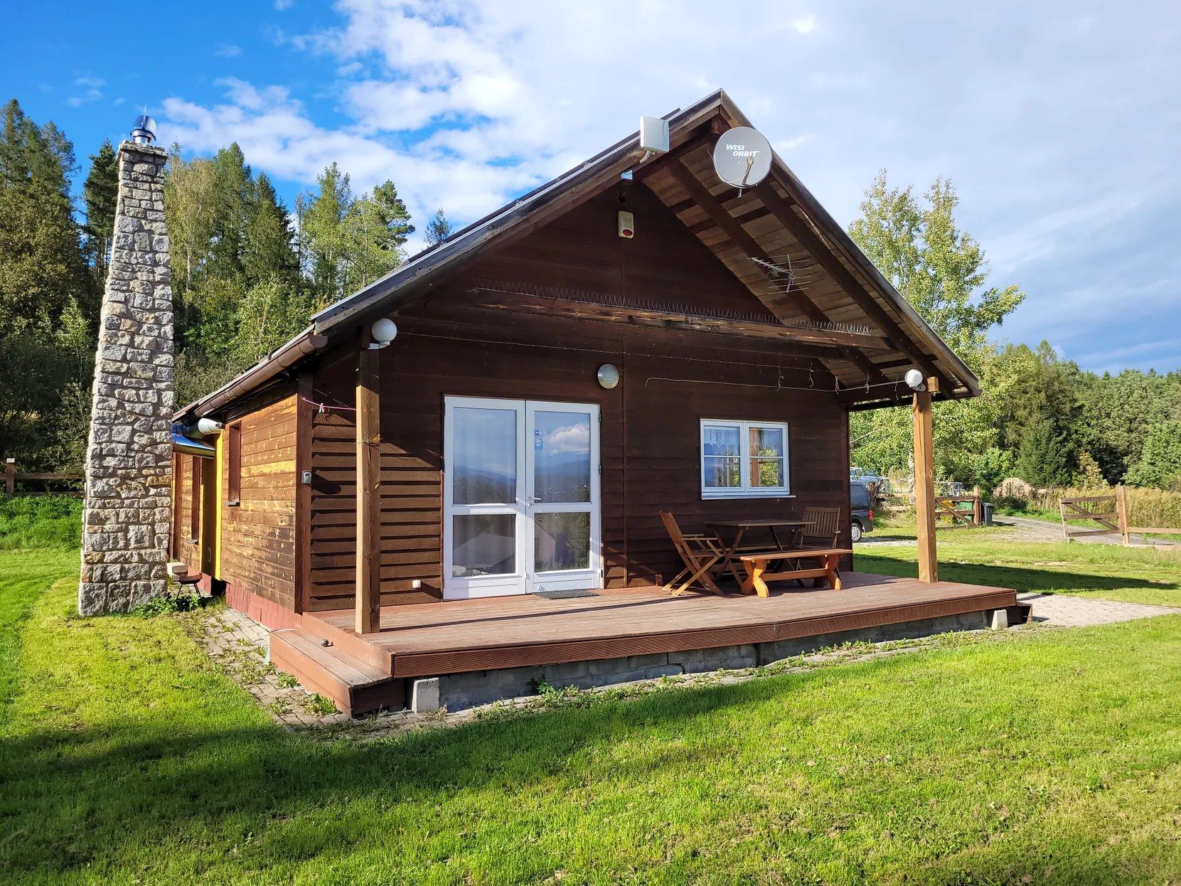 Une cabane en bois avec une cheminée en pierre, une véranda avec des sièges et une antenne parabolique.