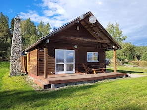 A wooden cabin with a stone chimney, a porch with seating, and a satellite dish. - Charming Hillside Cottage with Sauna (Wojcieszyce)