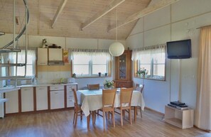 A spacious kitchen with wooden cabinets, a dining table with chairs, a television, and a window with curtains. - Charming Hillside Cottage with Sauna (Wojcieszyce)