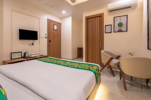 Una habitación de hotel con cama, escritorio, silla, televisor y puerta.