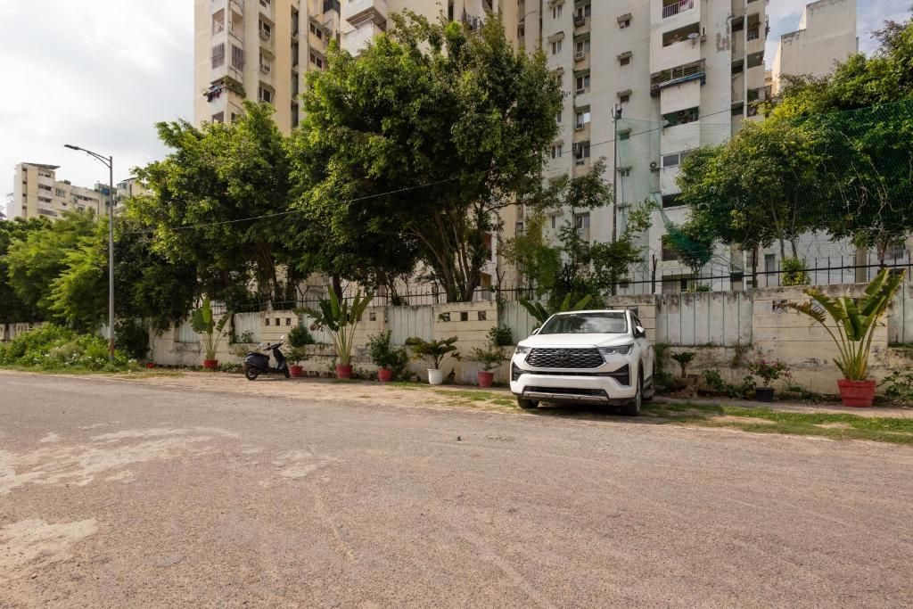 A residential area with a white car parked on the street, surrounded by trees and a fence.