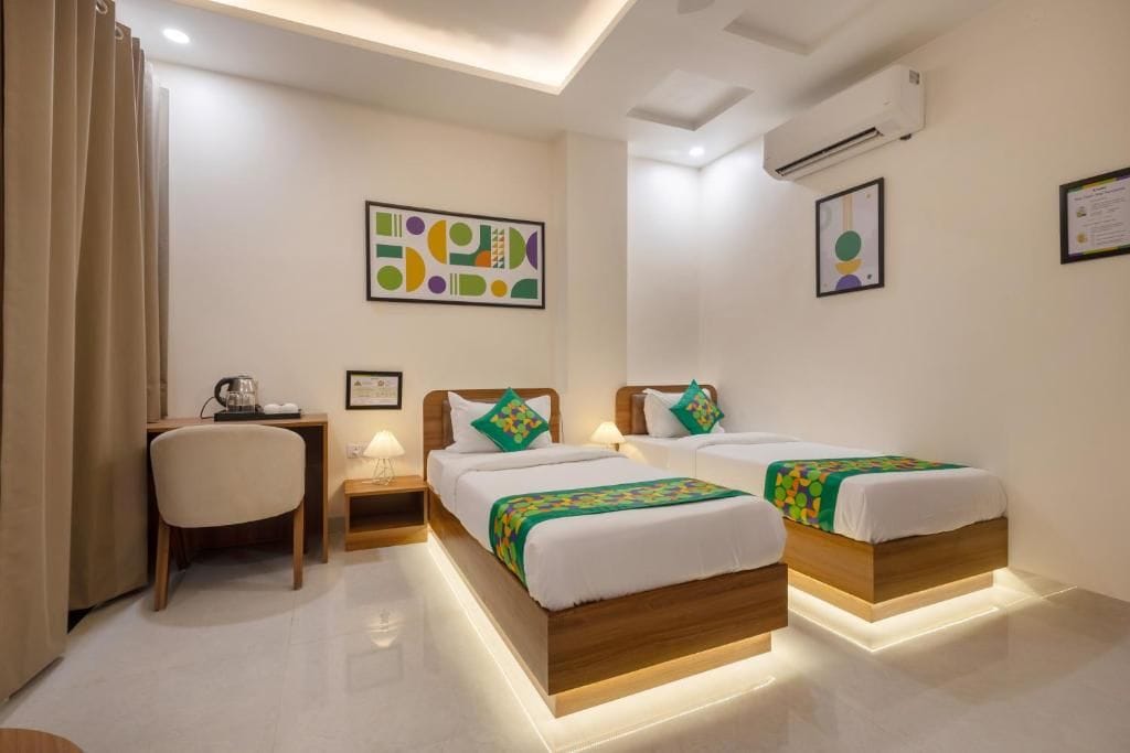 A hotel room with two beds, a desk, a chair, and a wall-mounted air conditioner.