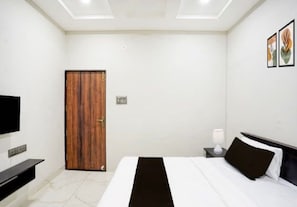 Una habitación de hotel con una cama, un televisor, una puerta de madera y una mesita de noche con una lámpara.
