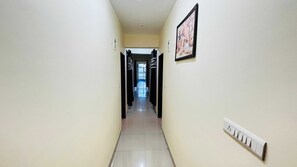 Un pasillo estrecho con suelo de baldosas, un interruptor de luz en la pared y un cuadro enmarcado.