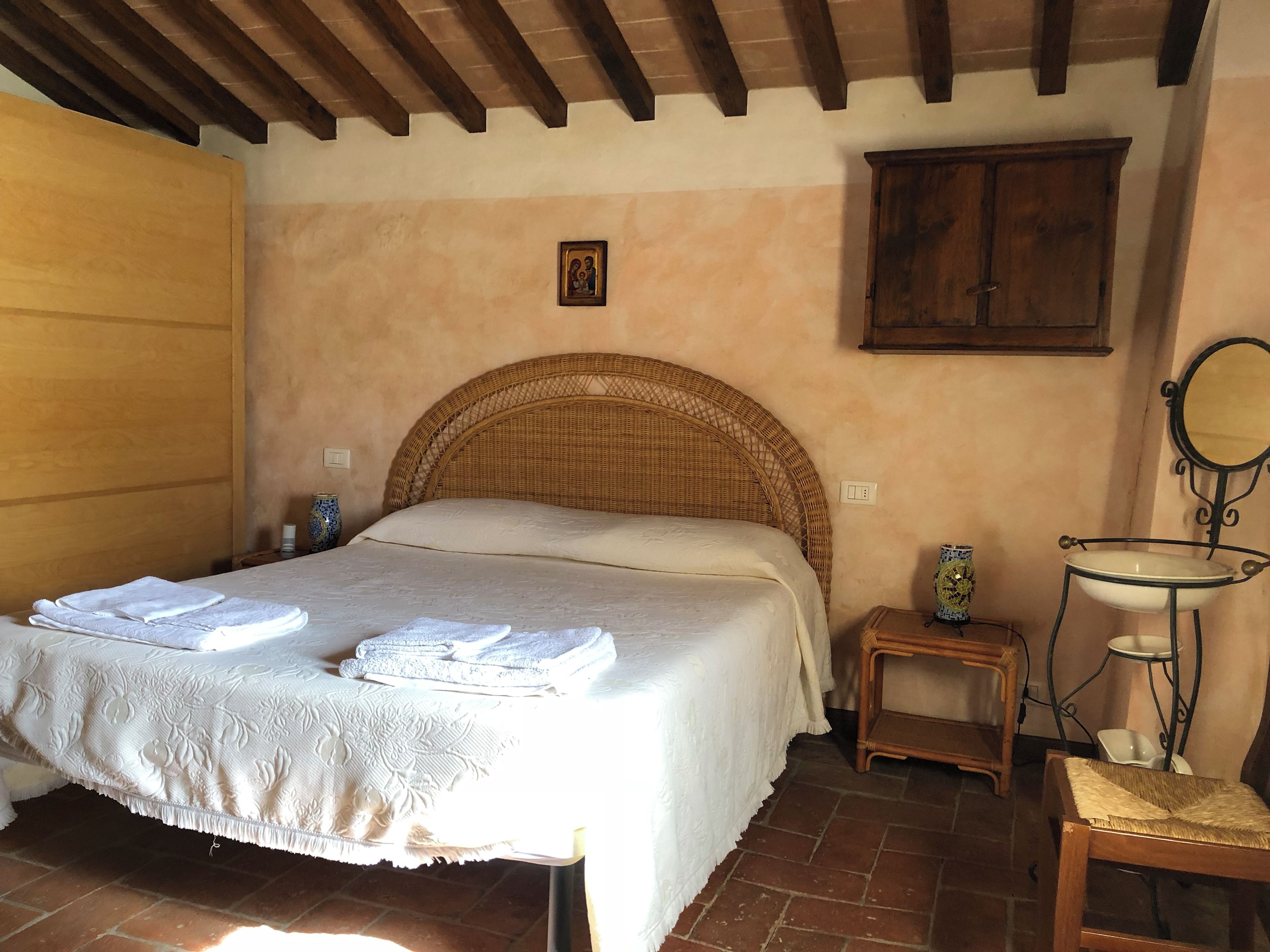 Quarto com uma cama grande, cabeceira de madeira, mesa de cabeceira pequena, uma cadeira, espelho e armário.