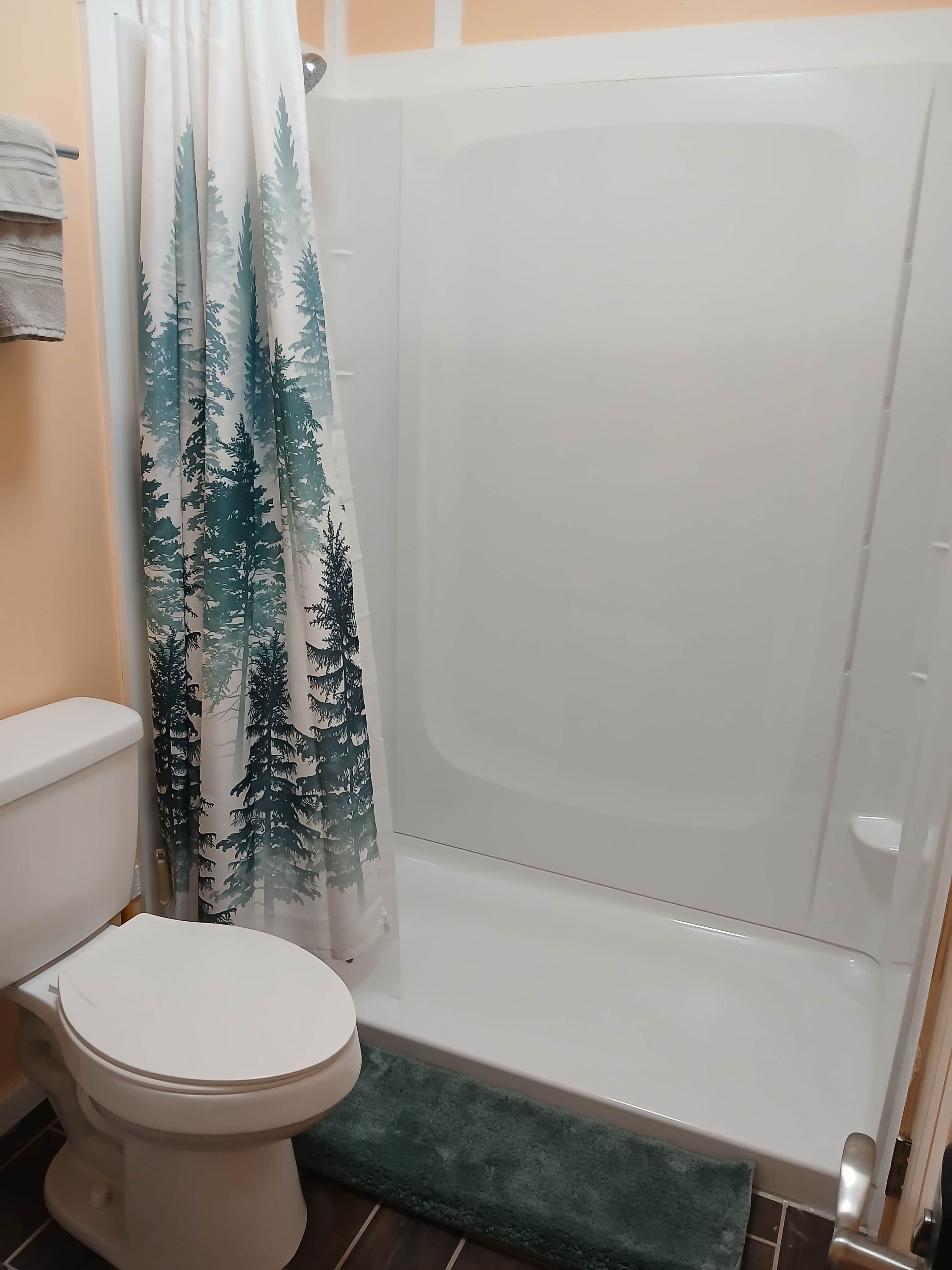 Un baño con inodoro, ducha con cortina de motivos forestales y alfombra de baño verde.