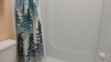 Un baño con inodoro, ducha con cortina de motivos forestales y alfombra de baño verde.