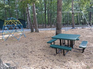 Un parque infantil con una estructura para escalar y mesas de picnic en un área boscosa.