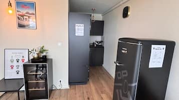 A compact living space with a kitchenette, a refrigerator, a dining table, and a wall-mounted light fixture.