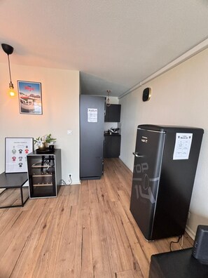 A compact living space with a kitchenette, a refrigerator, a dining table, and a wall-mounted light fixture. - Vrbo Property (Toulon)