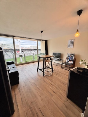 A modern living room with a large window, a dining area, and a TV. - Vrbo Property (Toulon)