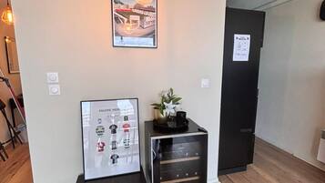 A room with a wooden floor, a black cabinet with drawers, a framed poster, a hanging light fixture, and a door with a sign.