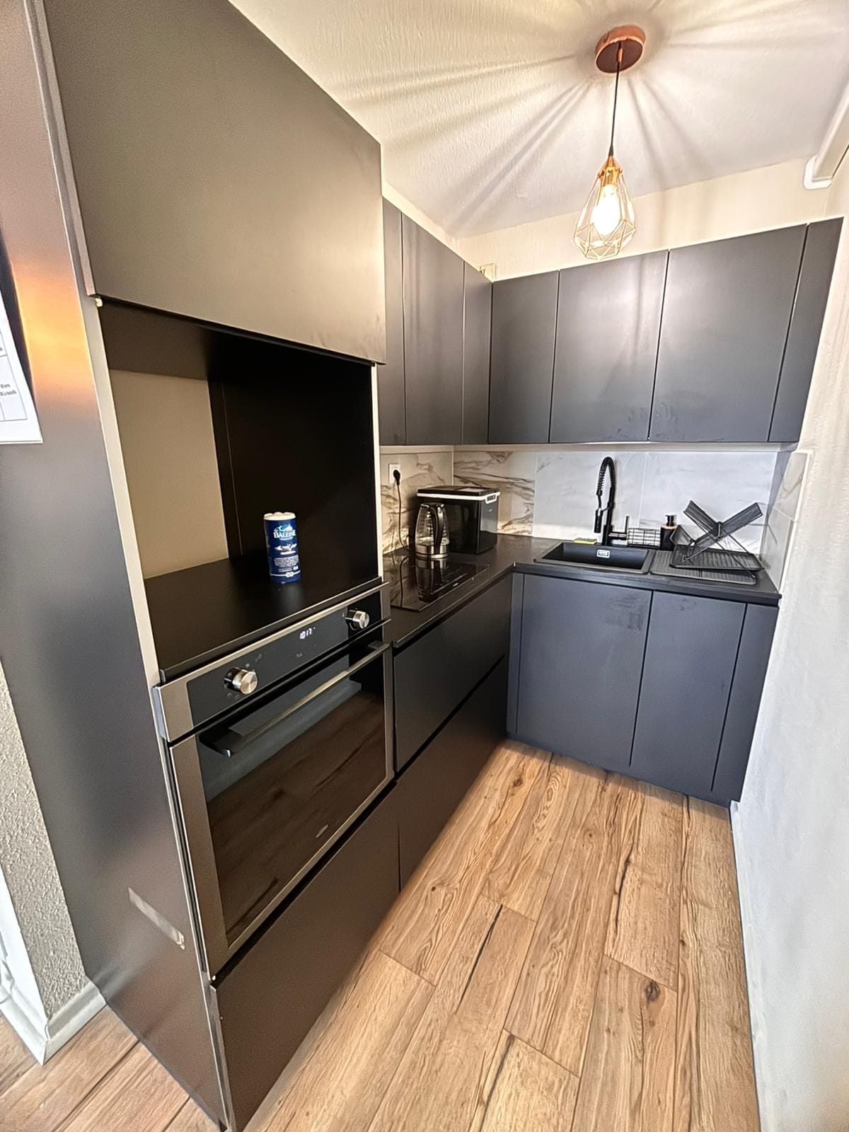 Una cocina moderna con electrodomésticos de acero inoxidable, piso de madera y una lámpara colgante.